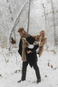 A happy couple having fun with a piggy back ride in a snowy winter forest, showcasing joy and love.