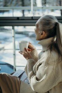 Woman in a cream sweater enjoying a moment of inner clarity and quiet authority while looking out a bright window.